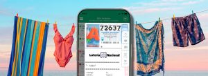 Móvil con décimo de Lotería Nacional sobre toallas de playa para jugar el sorteo extraordinario de vacaciones.