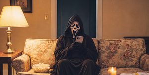 Persona con máscara de terror mirando el móvil en el sofá, para ilustrar cómo jugar siempre los mismos números de lotería sin sustos.